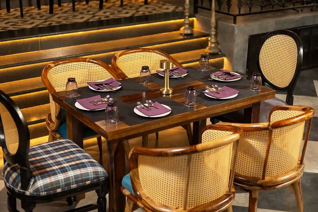 A wooden table laid for dinner, with cane chairs and tartan cushions