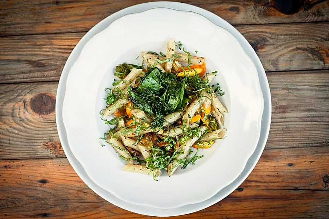 Pasta tossed with greens on a white plate, seen from above